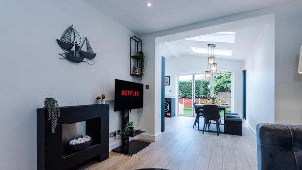 Ein modernes Wohnzimmer mit Kamin, Fernseher und Essbereich mit Tageslicht.