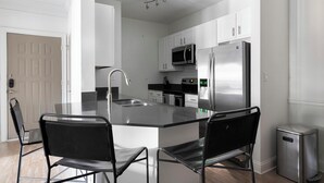 A modern kitchen with a central island, stainless steel appliances, and black chairs. - Landing | Spectacular 1BD, Game Room, Clubhouse (Buckhead)