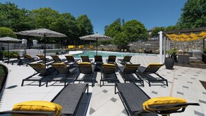 A poolside area with sun loungers and umbrellas, a pool, and a stone wall. - Landing | Spectacular 1BD, Game Room, Clubhouse (Buckhead)