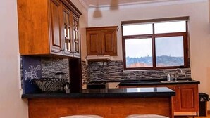 Una cocina con armarios de madera, encimera negra, dos taburetes de bar y luces colgantes.