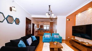 Una sala de estar moderna con un sofá negro, dos sillones azules, una mesa de centro de madera y un televisor grande.
