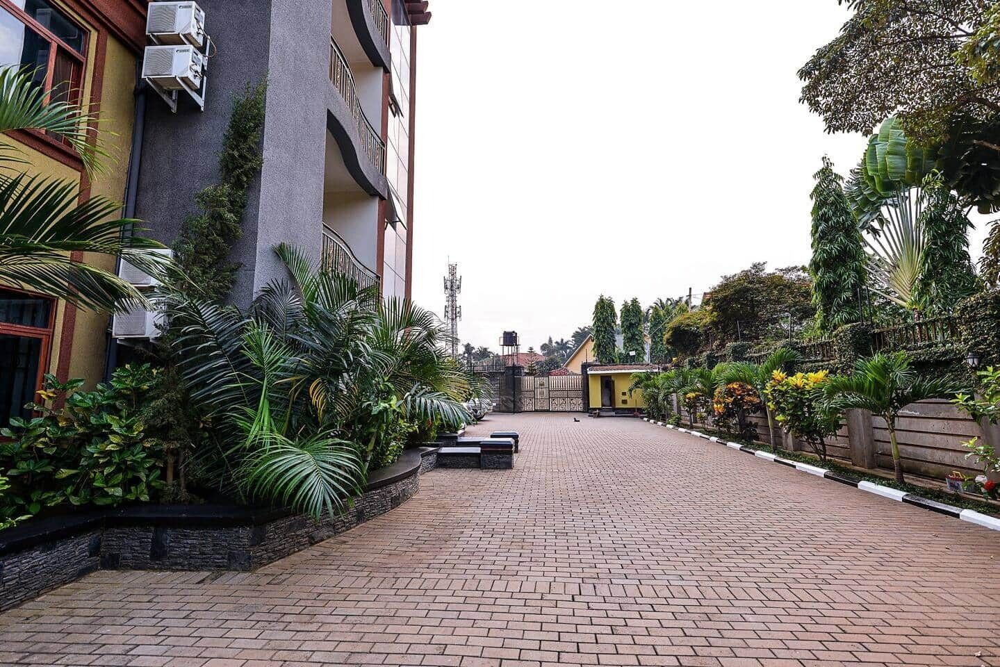 A paved courtyard with a building on one side and a variety of plants and trees on the other.