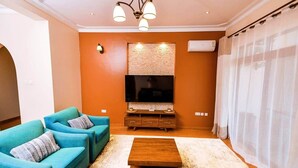 Un salón con un televisor de pantalla plana grande, sofás color turquesa, una mesa de centro de madera y una pared con textura.
