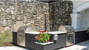 Cocina exterior con dos parrillas y jardinera integrada con flores.