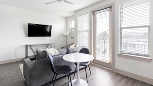 Ein modernes Wohnzimmer mit einem grauen Sofa, einem runden weißen Tisch und einem flachbildfernseher an der Wand.