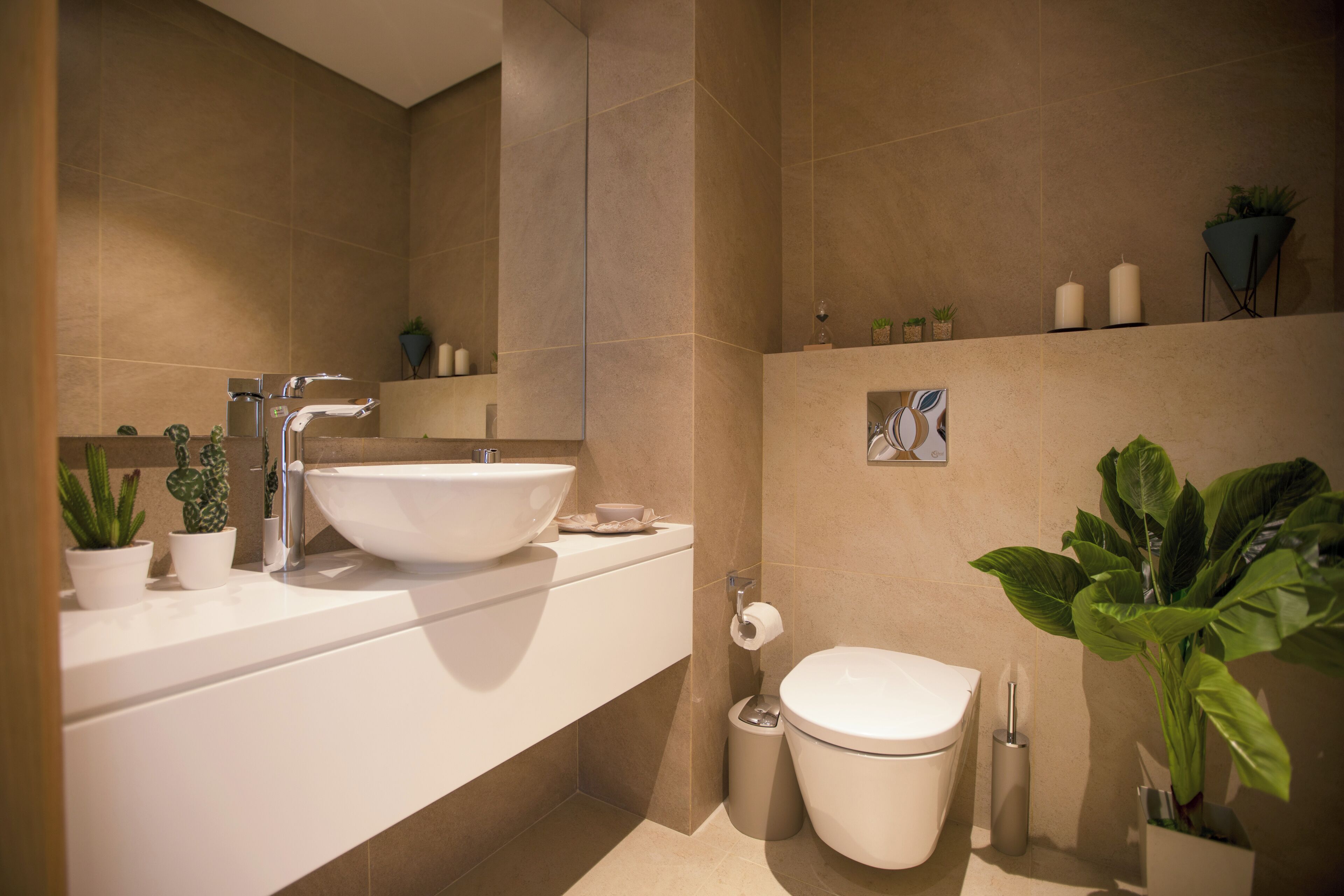 Un baño moderno con un lavamanos grande y blanco, un inodoro y varias plantas en macetas.