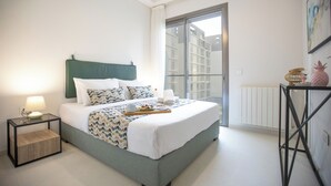 Een moderne slaapkamer met een groot bed, een nachtkastje met een lamp, en uitzicht buiten door een groot raam.