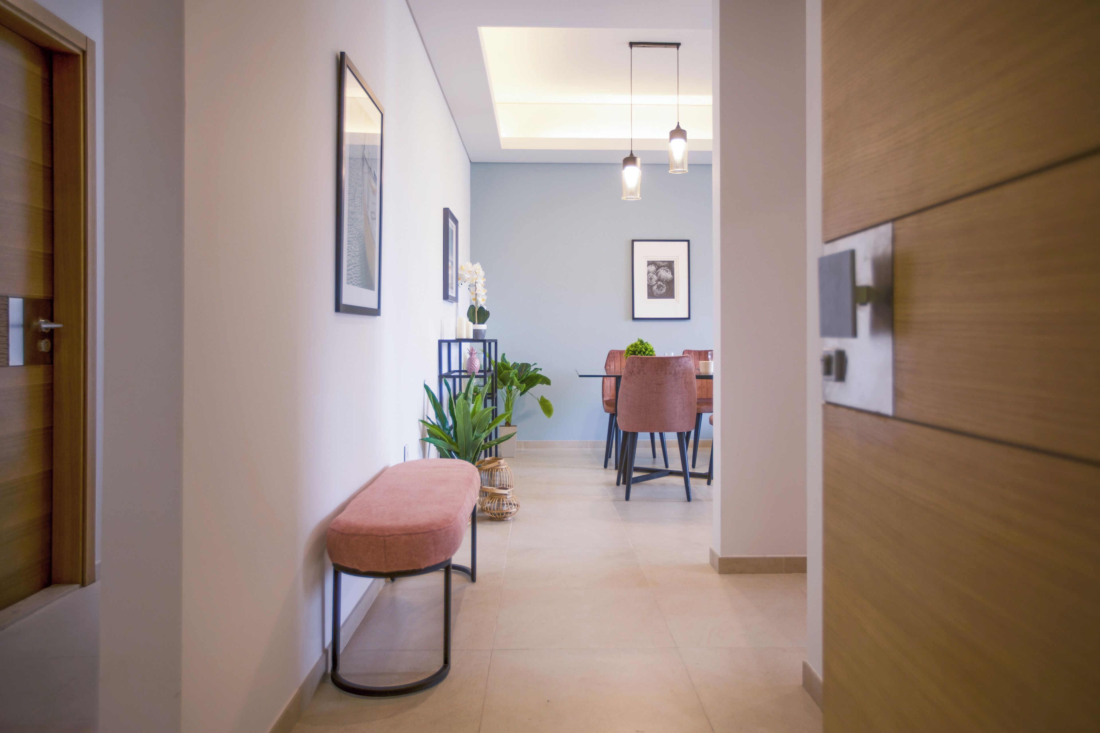 A hallway with a bench, a dining area with chairs and a table, and framed pictures on the walls.