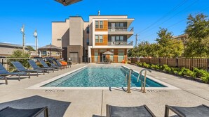 A modern building with a swimming pool, lounge chairs, and a fenced area. - Landing | Stunning Studio, Gym, Pool (Dallas)