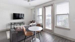 A modern living room with a grey sofa, two brown chairs, a white table, and a flat-screen TV mounted on the wall. - Landing | Stunning Studio, Gym, Pool (Dallas)