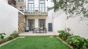 Un cortile con un piccolo prato, un tavolo e sedie, e un edificio con un balcone.