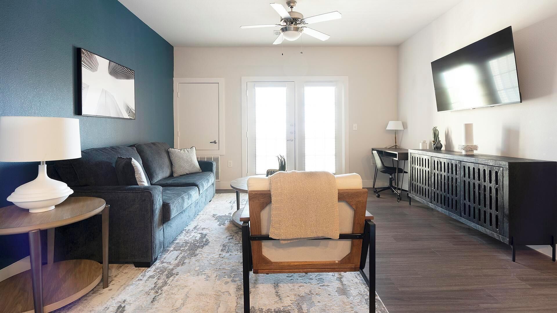 A modern living room with a sofa, armchair, coffee table, and a TV mounted on the wall.