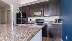 A modern kitchen with dark wood cabinets, stainless steel appliances, and granite countertops. - Landing | Incredible 1BD, Tennis Court, Gym (Fort Myers)