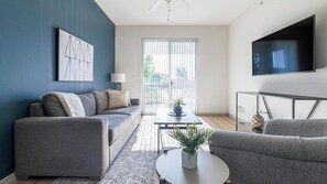 A modern living room with a grey sofa set, a coffee table, and a TV mounted on the wall. - Landing | Incredible 1BD, Tennis Court, Gym (Fort Myers)