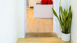 Ein Flur, der zu einem Raum führt, mit einem weißen Schrank, einem roten Kissen auf einem weißen Sofa und einer Zimmerpflanze.