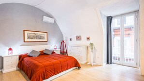 Ein Schlafzimmer mit einem Bett, Nachttischen, einem Schminktisch, einem Fenster mit Vorhängen und einer Wand-Klimaanlage.