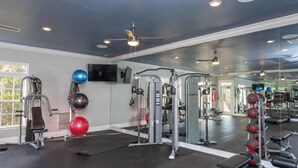 Ett gym med olika typer av träningsredskap, en takfläkt och en stor spegel.