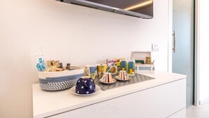 A modern kitchen with a white countertop, a kettle, a coffee maker, and a bowl of snacks. - RELAIS ROMA BEACH (Fiumicino)