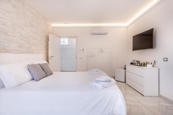 A modern bedroom with a bed, a dresser, a TV, and a walk-in closet. - RELAIS ROMA BEACH (Fiumicino)