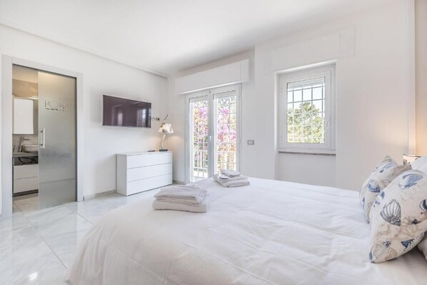 A modern bedroom with a large bed, a bedside table with a lamp, and a view through a glass door. - RELAIS ROMA BEACH (Fiumicino)