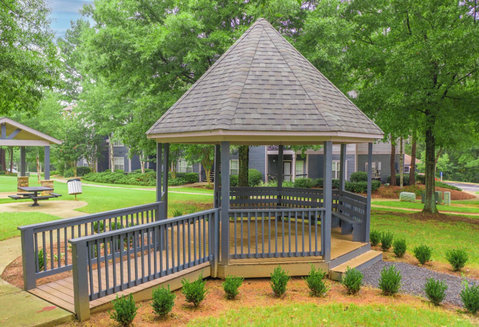 A gazebo with a wooden deck and railings, surrounded by a well-maintained lawn and trees.
