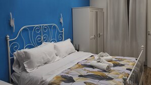 Ein Schlafzimmer mit einem Bett, weißen Vorhängen, einem Kleiderschrank und einer blauen Wand.