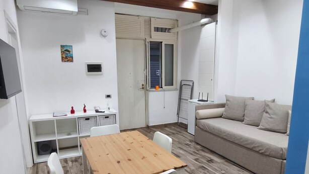 Ein modernes Wohnzimmer mit einem Holzesstisch, weißen Stühlen, einem beigen Sofa und einem an der Wand montierten Fernseher.