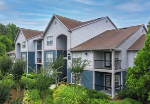A multi-story residential building with a balcony on the second floor, surrounded by greenery.