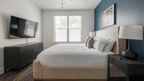 A bedroom with a bed, a dresser, a TV, a window with blinds, and a lamp.