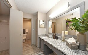 A modern bathroom with a granite countertop, a large mirror, and a potted plant. - Landing | Modern 1BD, Pool, Clubhouse (Huntsville)