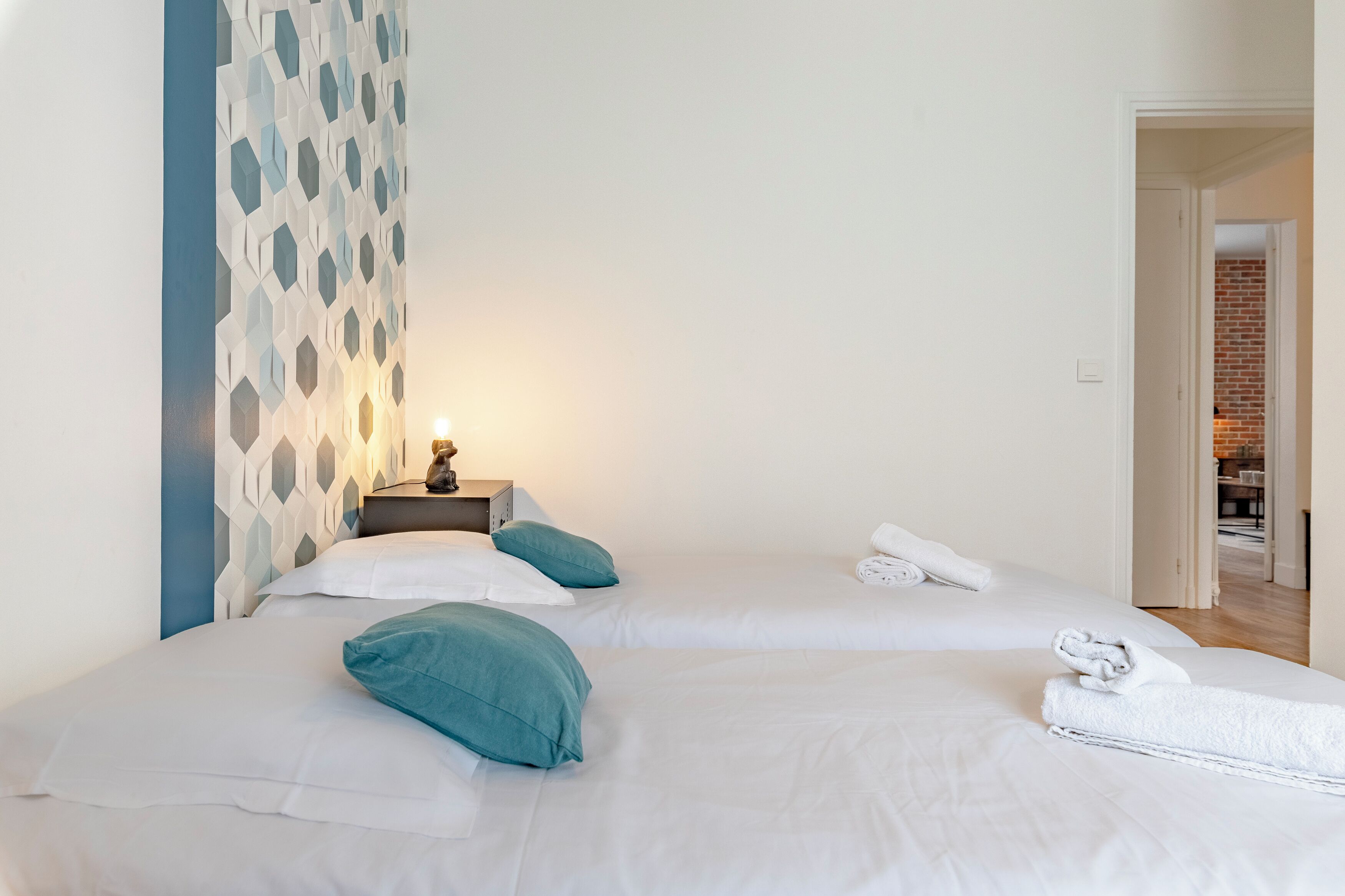 Ein Hotelzimmer mit zwei Betten, einem Nachttisch mit Lampe und einer Wand mit geometrischem Muster.