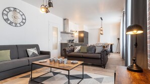 Uma sala de estar moderna com um sofá, uma mesa de centro e uma área de jantar ao fundo.