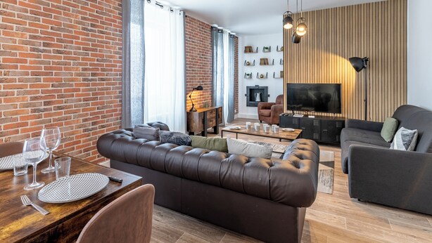 Uma sala de estar moderna com parede de tijolos, sofá de couro, mesa de jantar e televisão de tela plana.