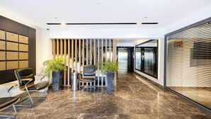 Un vestíbulo moderno con piso de mármol, zona de estar con sillones, plantas en macetas y un mostrador de recepción.