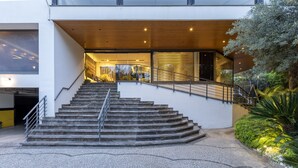 Un edificio moderno con una escalera que conduce a una entrada, un área pavimentada y algo de vegetación.