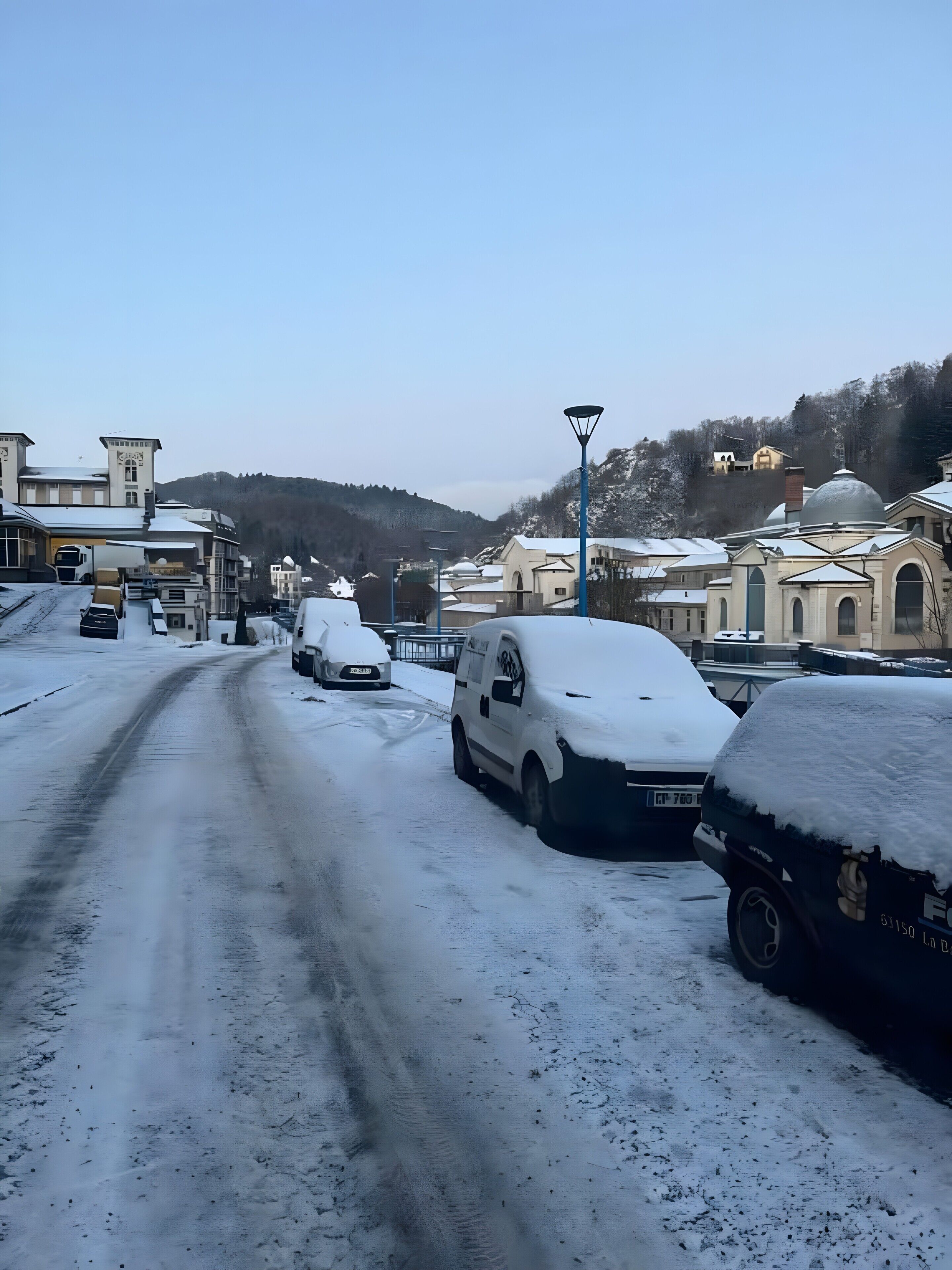 Een besneeuwde straat met geparkeerde auto's en gebouwen op de achtergrond.