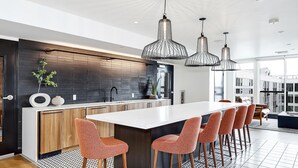 Uma cozinha moderna com ilha central, iluminação pendente e área de estar com cadeiras.