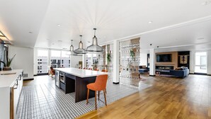 Uma sala de estar ampla com uma cozinha aberta grande, uma área de jantar com cadeiras laranja e um espaço de estar aconchegante com lareira.