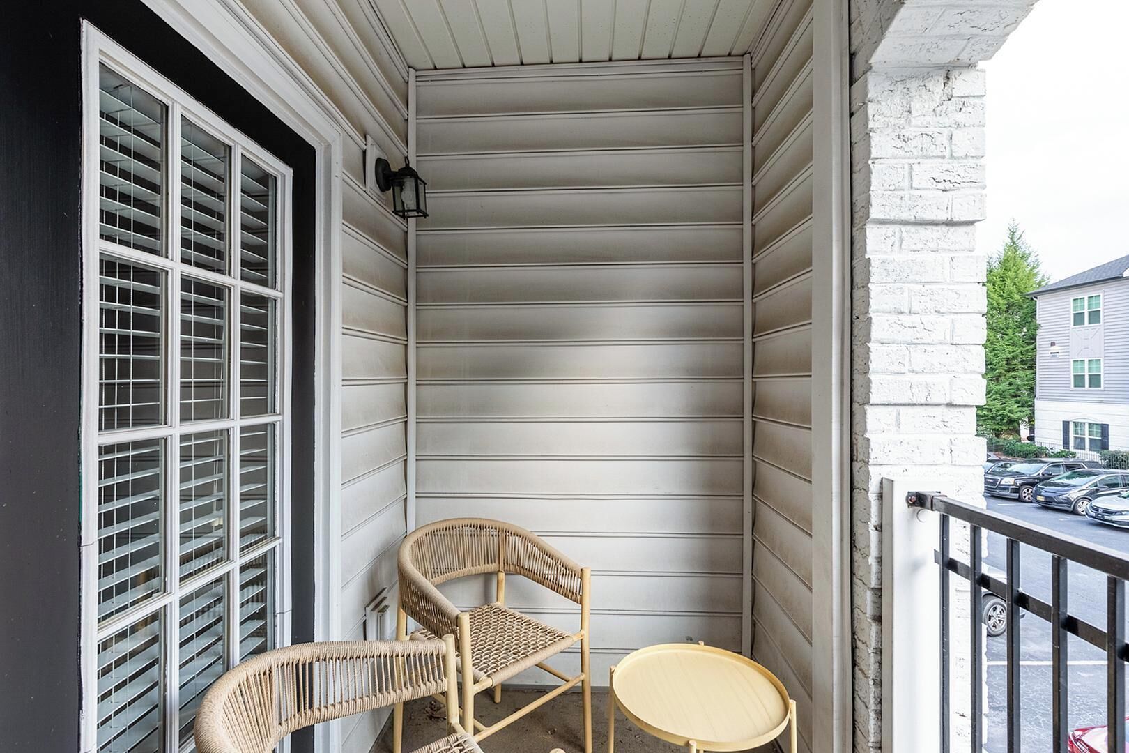 A corner balcony with white siding, a wicker chair, and a small round table.