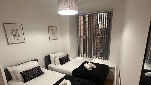 A modern bedroom with two beds, a ceiling light, and a window with blinds. - Stunning 2 Bed 2 Bath City Centre Apartment Liverpool (Liverpool)