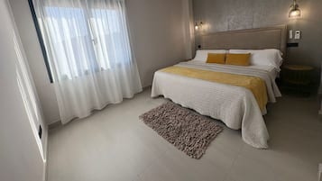 Una camera da letto moderna con un letto grande, un ventilatore a soffitto e vista sull'esterno attraverso tende leggere.