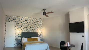 Un dormitorio con cama, escritorio con silla, ventilador de techo y televisor montado en la pared.