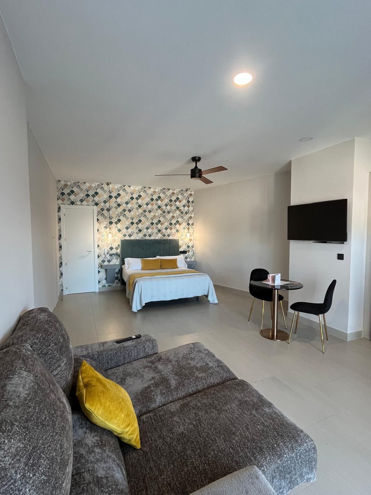 Una habitación de hotel moderna con cama, sofá, televisor y ventilador de techo.