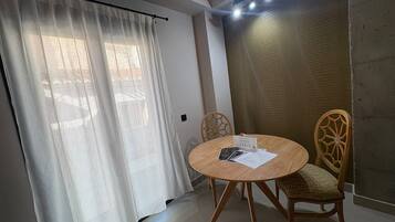 Una habitación con una mesa redonda de madera, dos sillas de mimbre, una cortina blanca y una pared con textura.