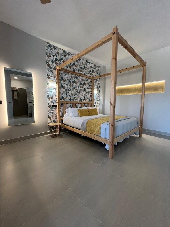 A modern bedroom with a four-poster bed, a round side table, and a patterned wallpaper. - LA LIPA SUITES (Almáchar)