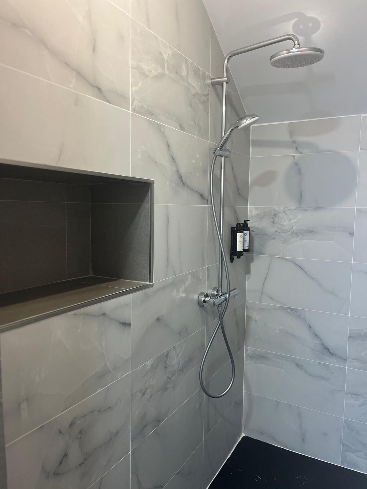 Un baño moderno con baldosas de mármol, un estante empotrado y una ducha con cabezal de ducha de mano.