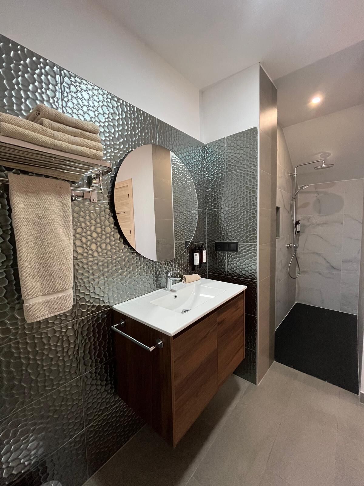 A modern bathroom with a large mirror, a white sink, wooden cabinets, and a shower area.