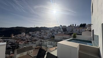 Vista desde un balcón que domina un pueblo costero con edificios blancos, cielo despejado y sol brillante.