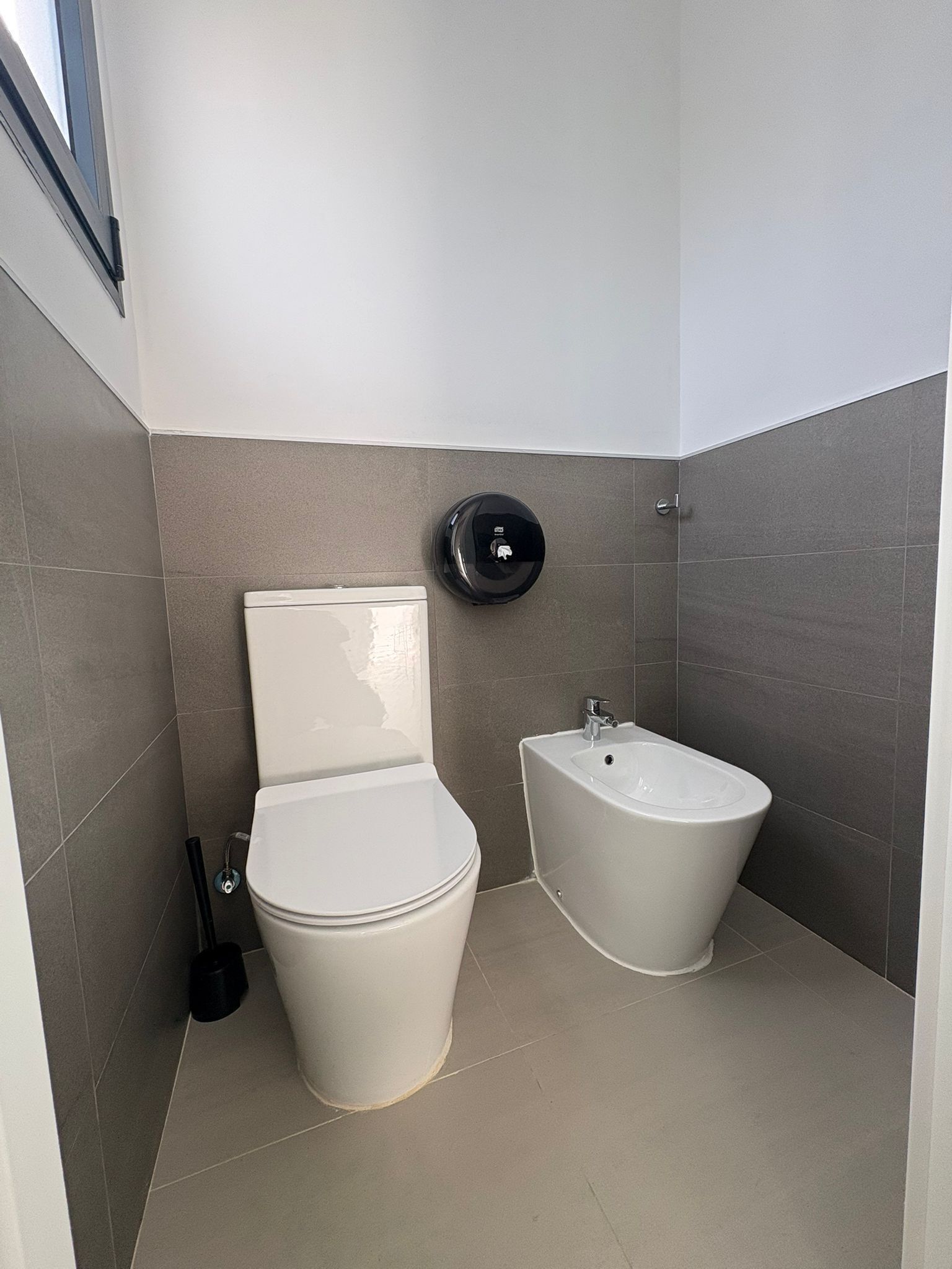 Un baño moderno con inodoro, bidé y dispensador de gel antibacterial.