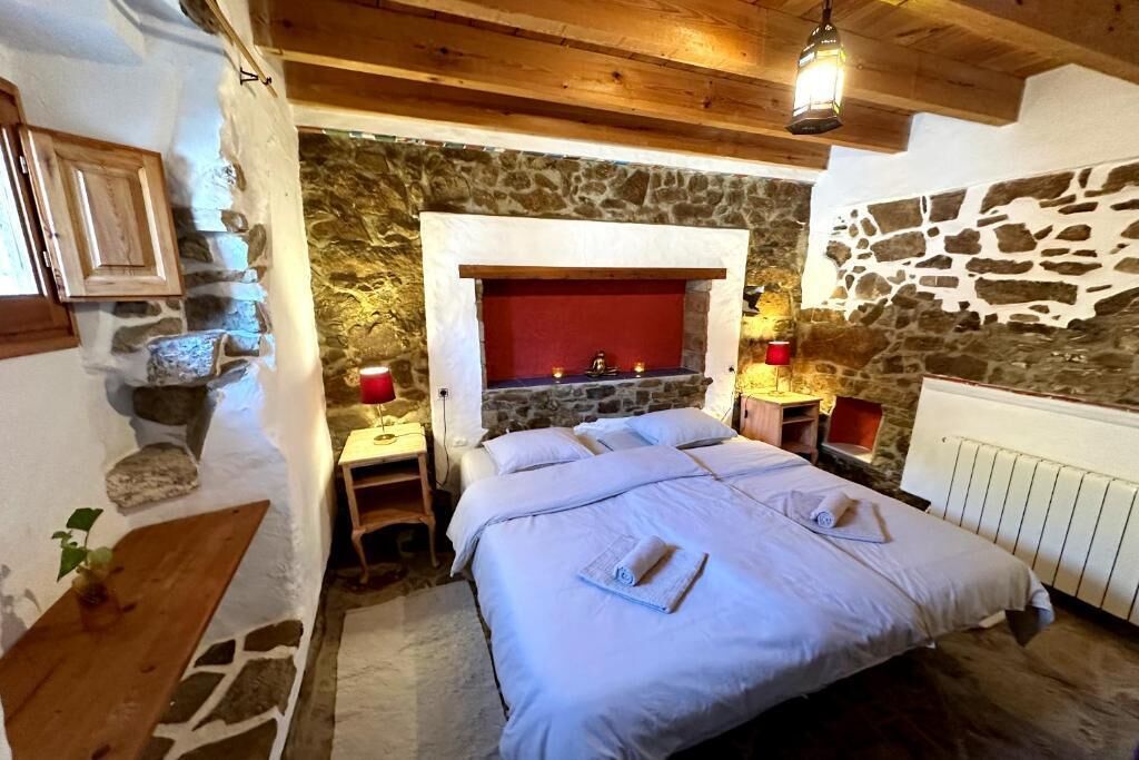 A bedroom with a stone wall, a fireplace, a bed with white linens, and wooden furniture.